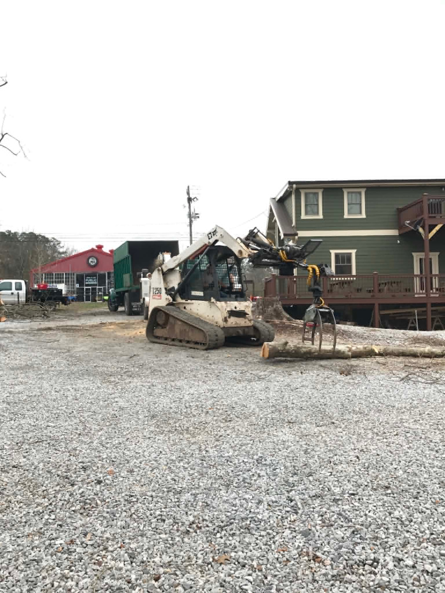 Skid steer with a grapple loading logs into the dump truck during cleanup