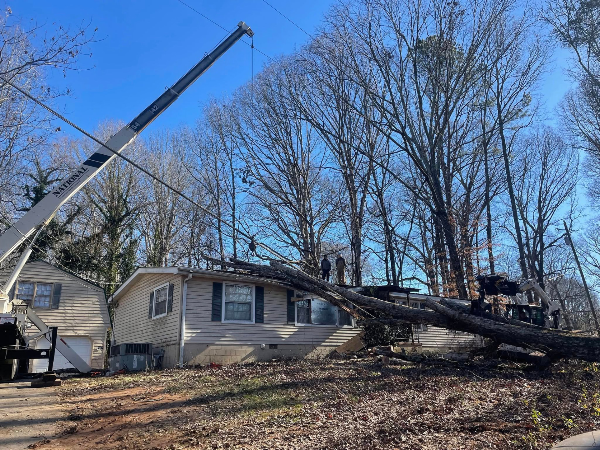National crane lifting a large fallen tree off a residential home during emergency storm cleanup
